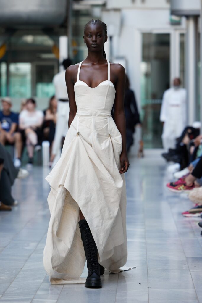 An asymmetric beige cotton sleeveless dress with a flowing silhouette and unique draping details.