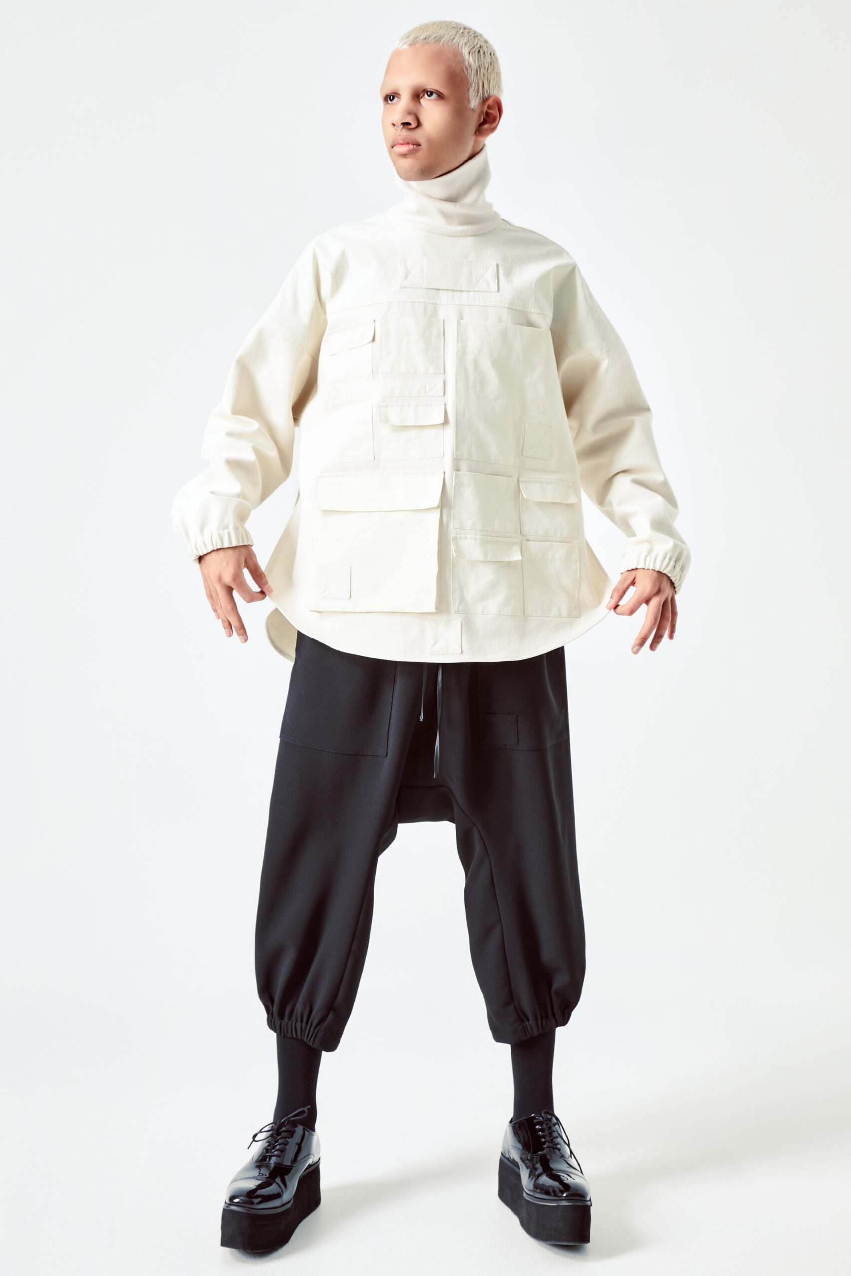 This relaxed top features a high-neck design and multiple pockets, offering a utilitarian edge. Paired with black pants that taper at the ankle, the ensemble balances structure and comfort, creating a modern silhouette.