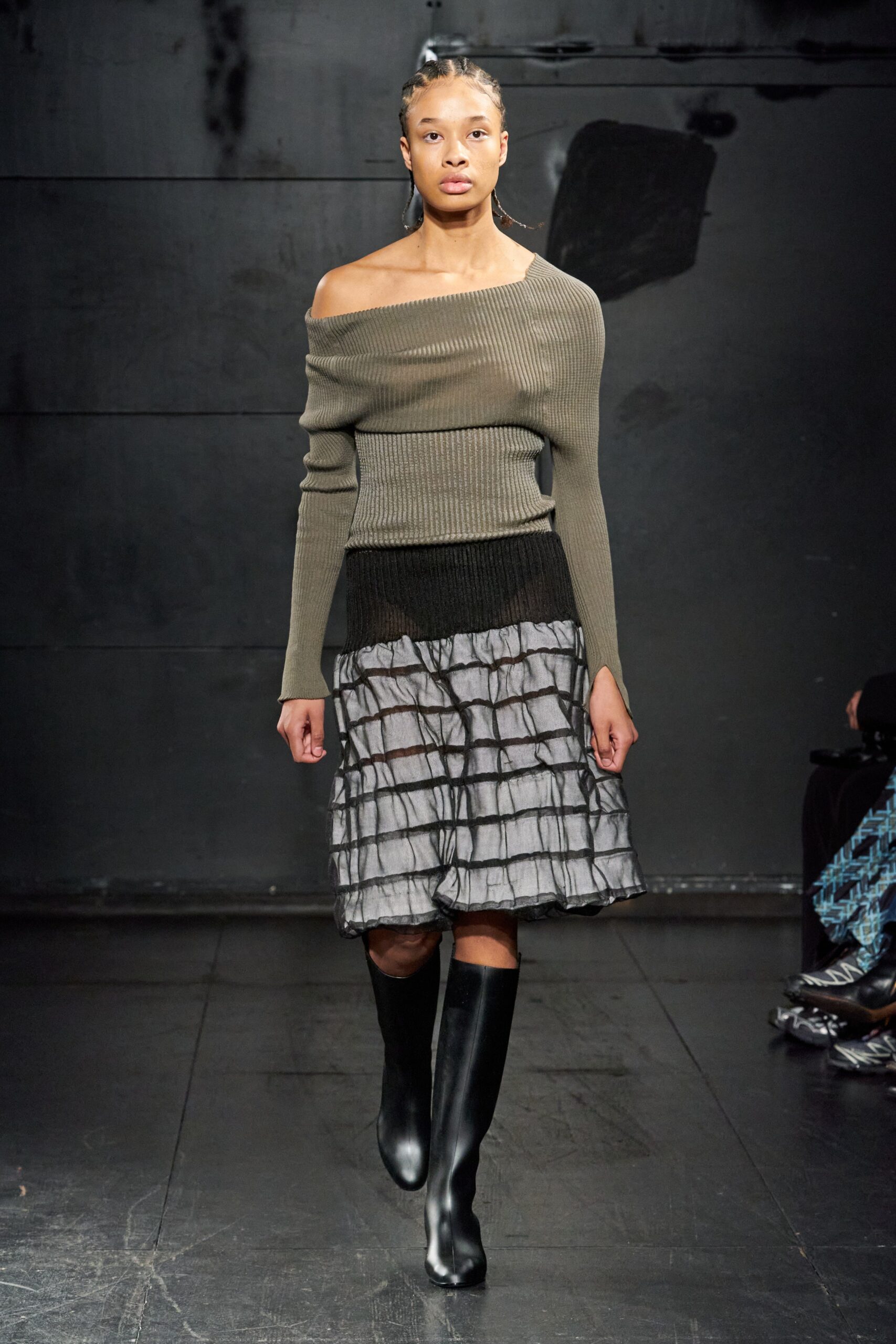 A fitted green long-sleeve top with an off-shoulder design paired with a pleated layered skirt.