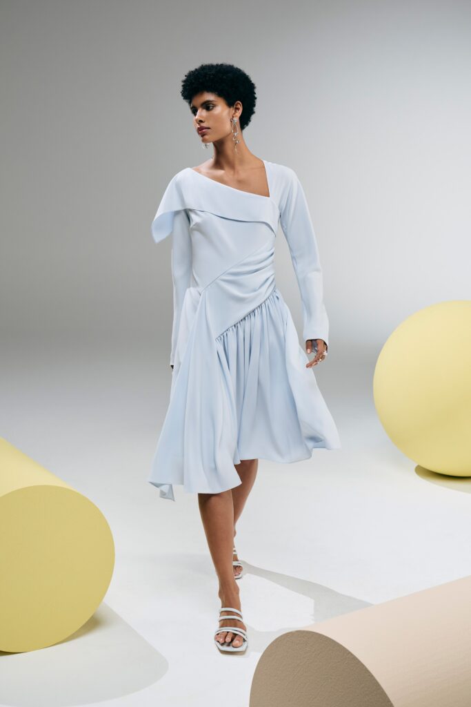 A fitted blue silk dress with long sleeves, a V-neckline, and an asymmetric draped design.