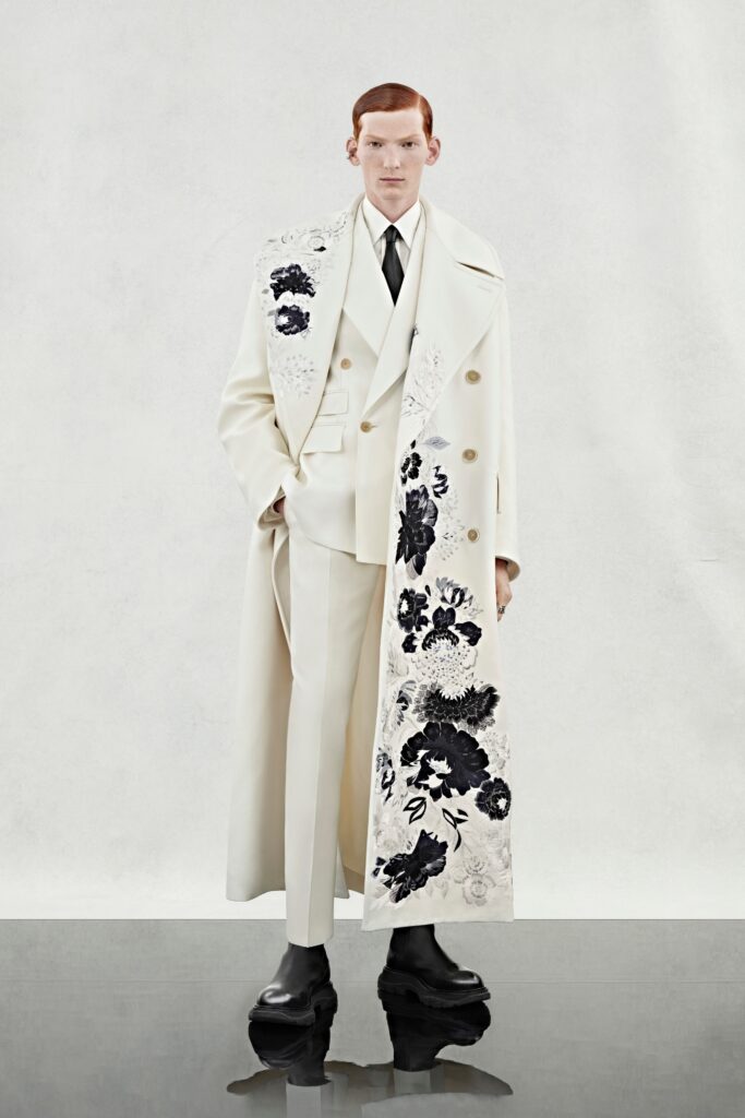 A tailored white coat with embroidered details worn over a matching suit.