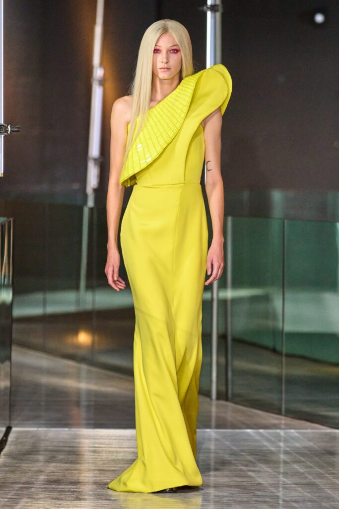 A fitted yellow silk dress with an asymmetric design and sleeveless high-neck construction.