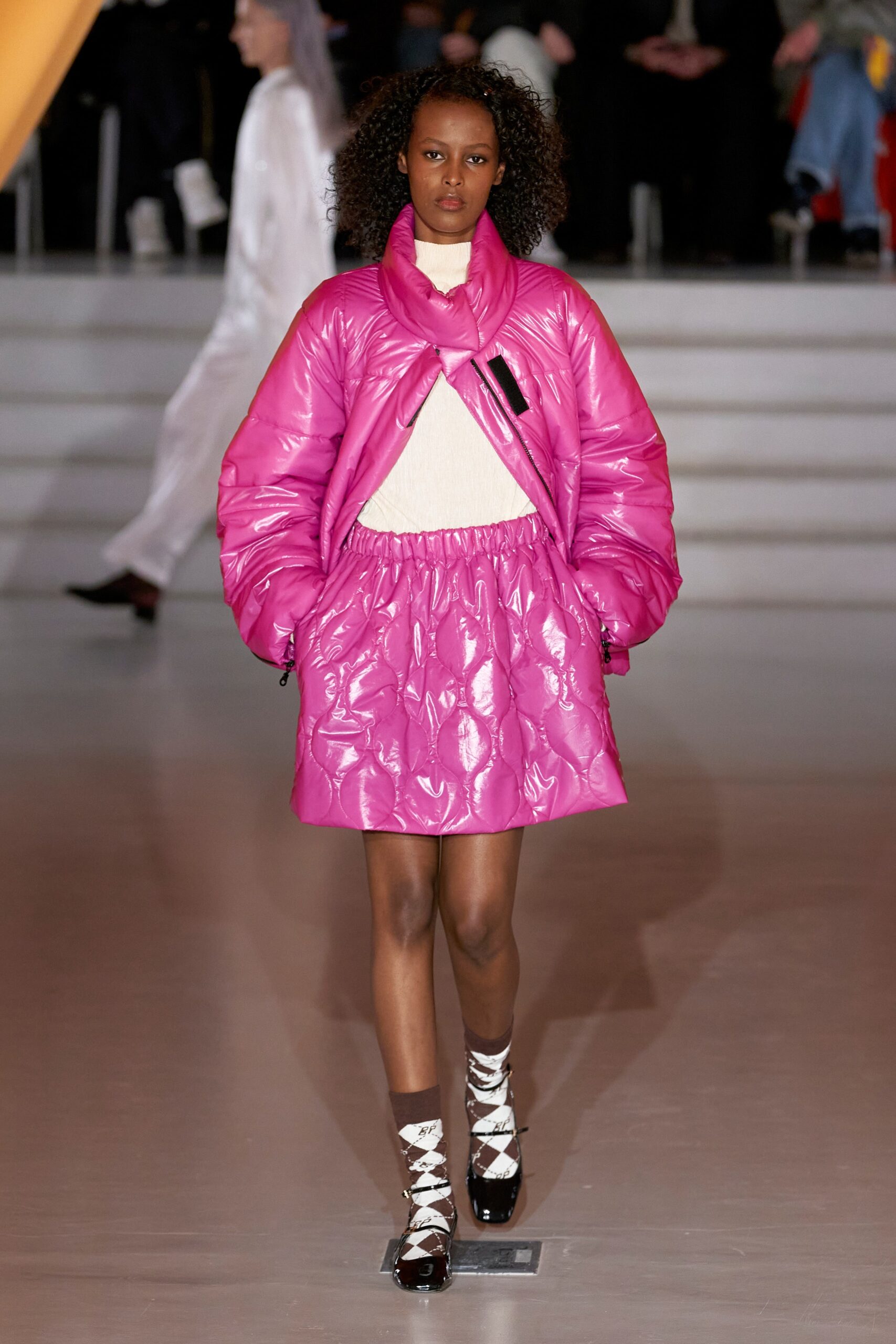 A relaxed pink puffer jacket with a collared neckline paired with a pleated skirt.