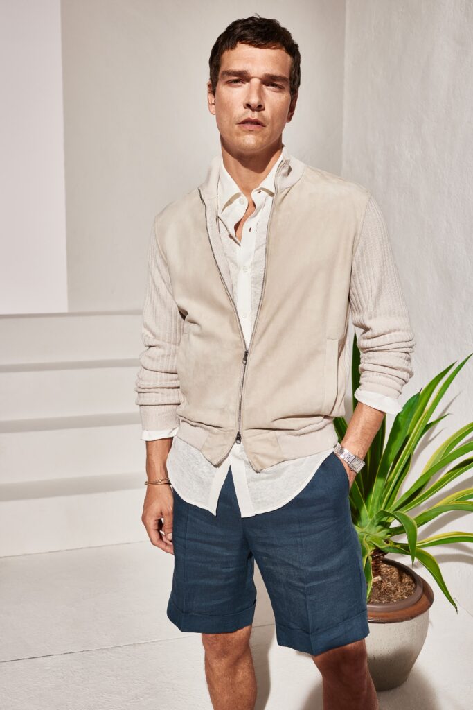 A relaxed beige suede jacket layered over a white collared shirt and blue shorts.