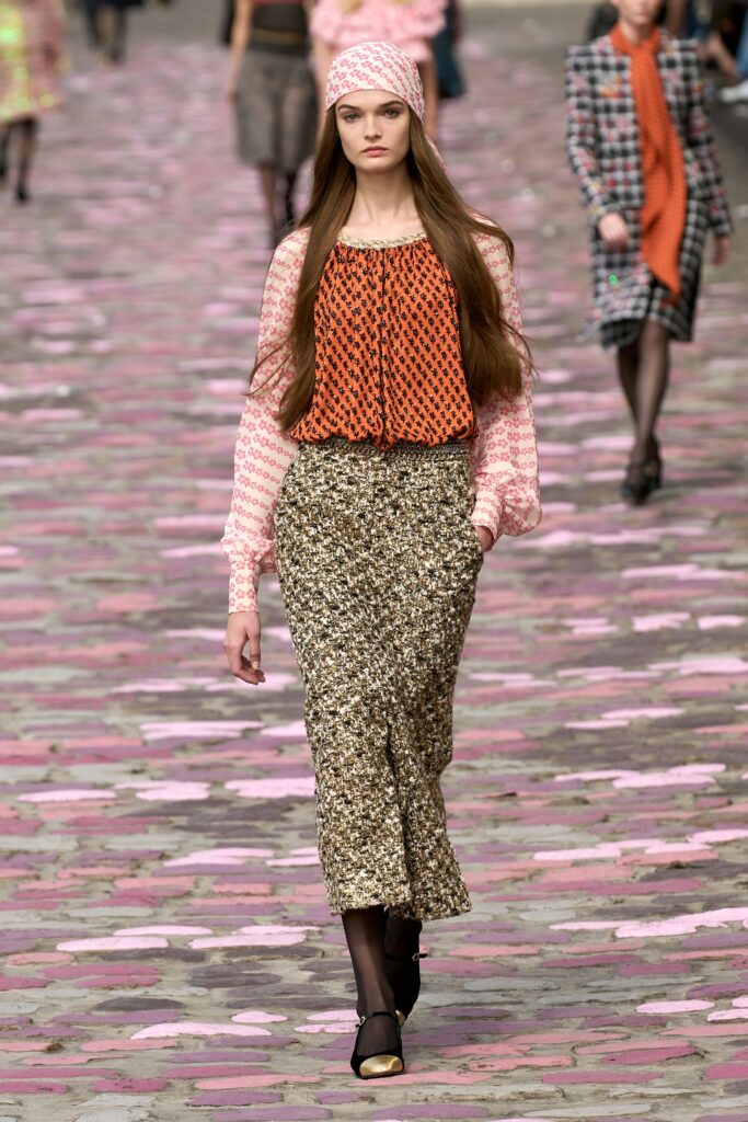 A relaxed pink printed top with long sleeves paired with a pleated brown skirt.