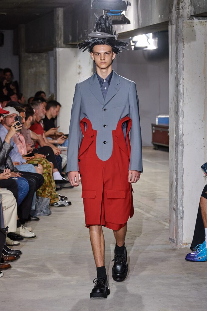 A relaxed gray coat with long sleeves and a collared design, paired with asymmetric red shorts.