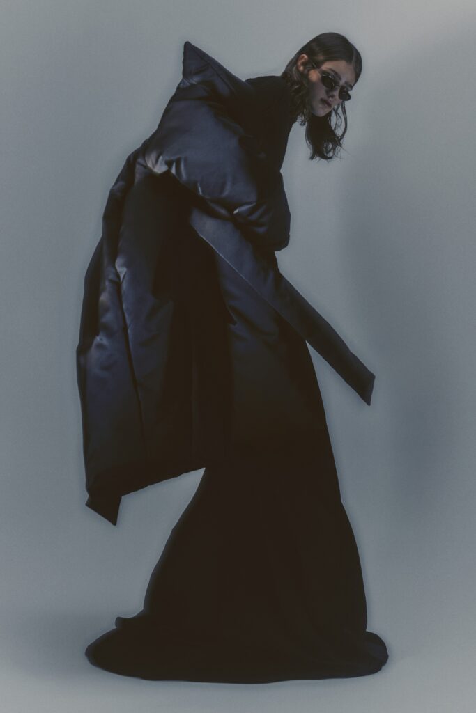 A fitted black silk dress with a long-sleeve coat and asymmetric design elements.