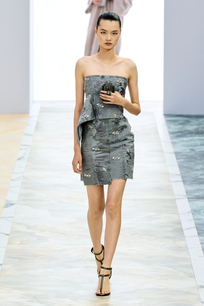 A fitted gray silk strapless dress with an asymmetric design detail.