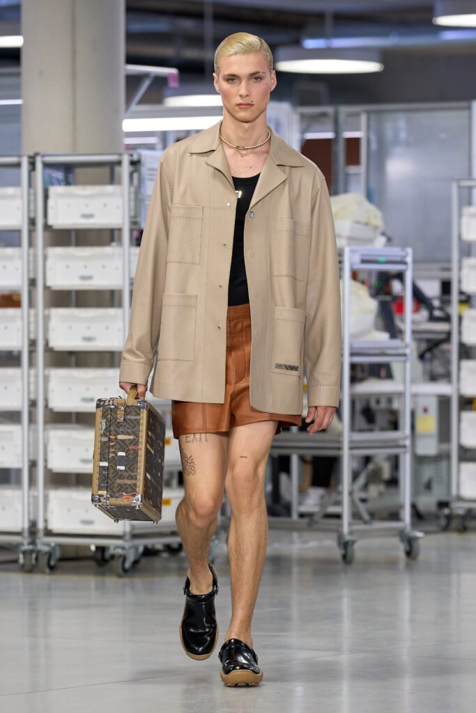 A fitted beige cotton shirt with a collared neckline paired with brown leather shorts.