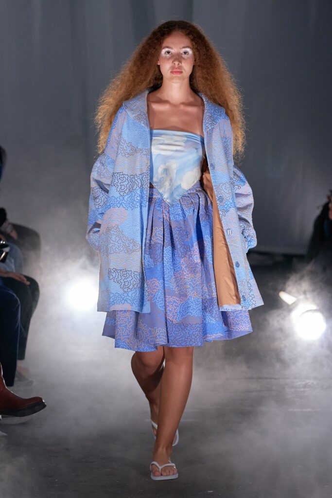 A relaxed blue printed sleeveless dress with a collared coat layered over it.