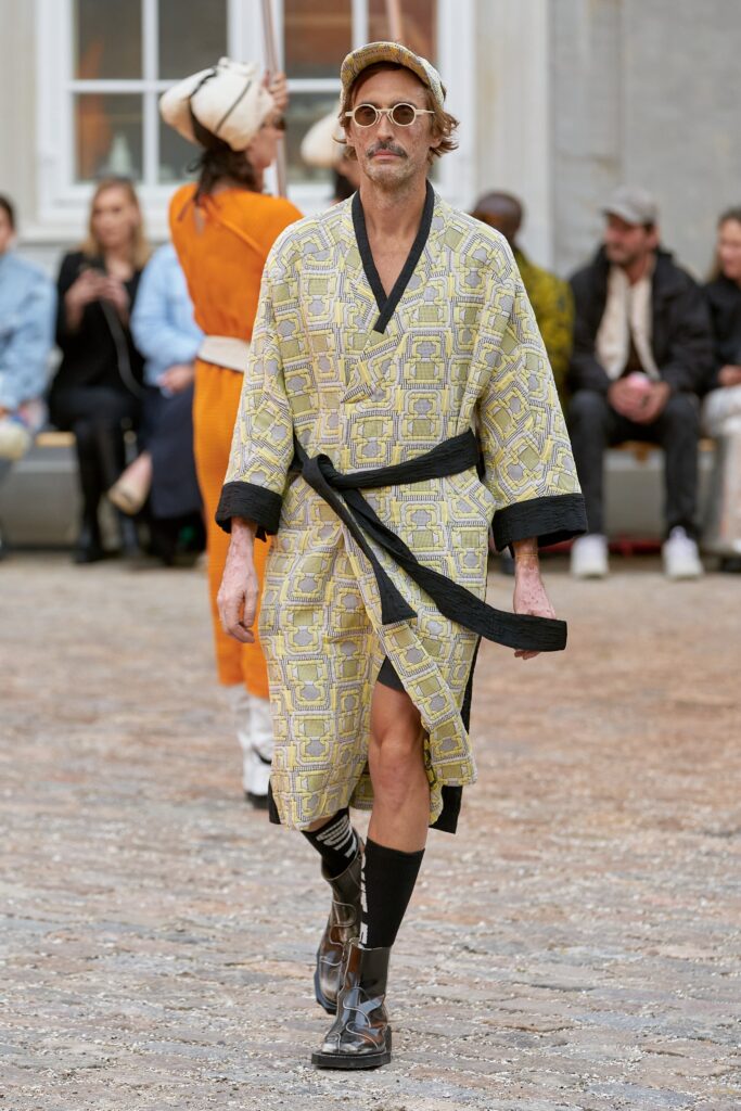 This relaxed robe features a vibrant yellow print that adds a playful touch to its silhouette. The long sleeves and belted waist enhance its casual yet stylish appeal, making it a standout piece on the runway.