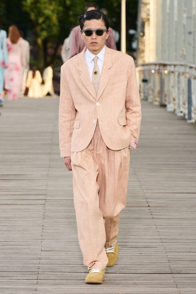A relaxed beige cotton suit with long sleeves, a collared shirt, and wide-leg trousers.