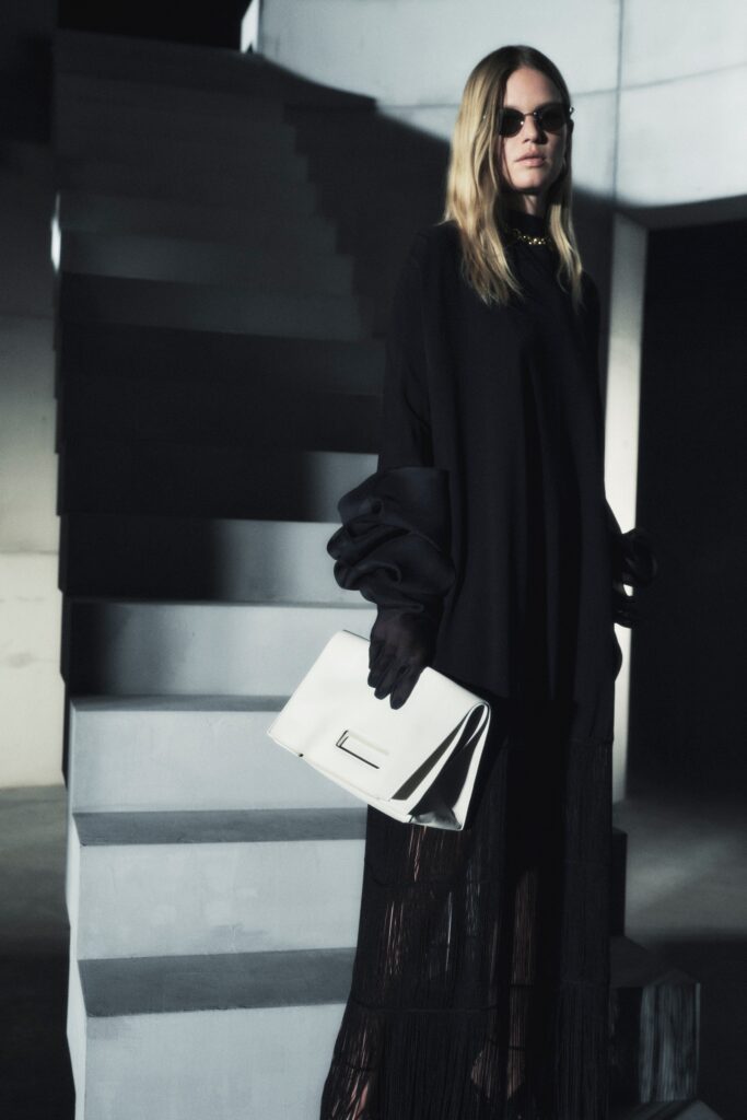 An oversized black silk dress with long sleeves, a high neckline, and fringed details.