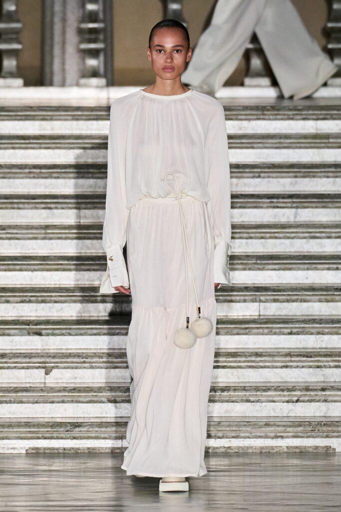 A relaxed white silk dress with long sleeves and a high neckline featuring a tiered design.