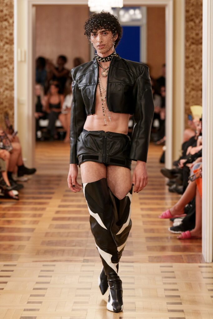 A fitted black leather sleeveless jacket paired with matching shorts, showcasing a bold fashion statement.