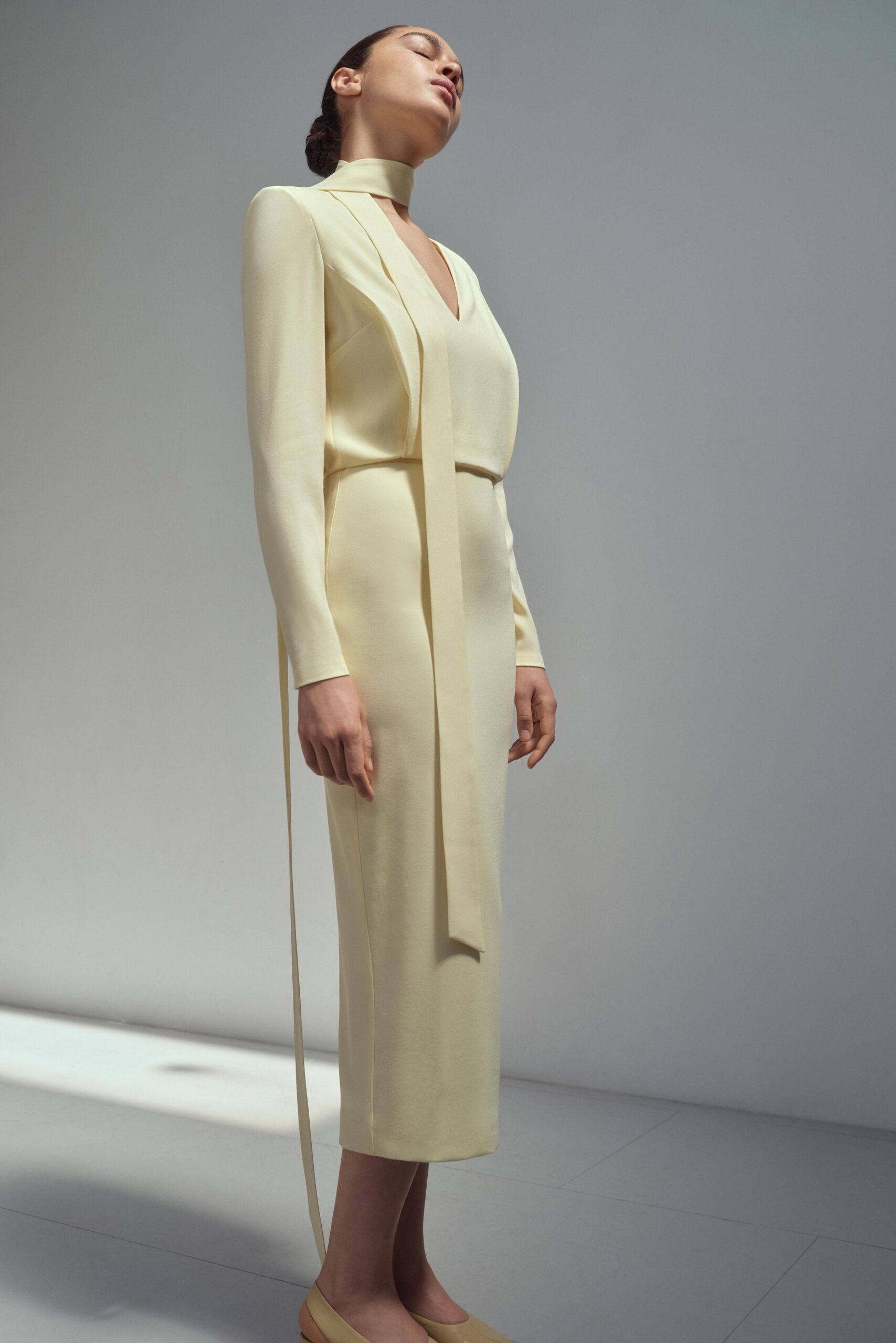 A fitted yellow silk dress with long sleeves and a V-neckline, featuring a straight-leg silhouette.