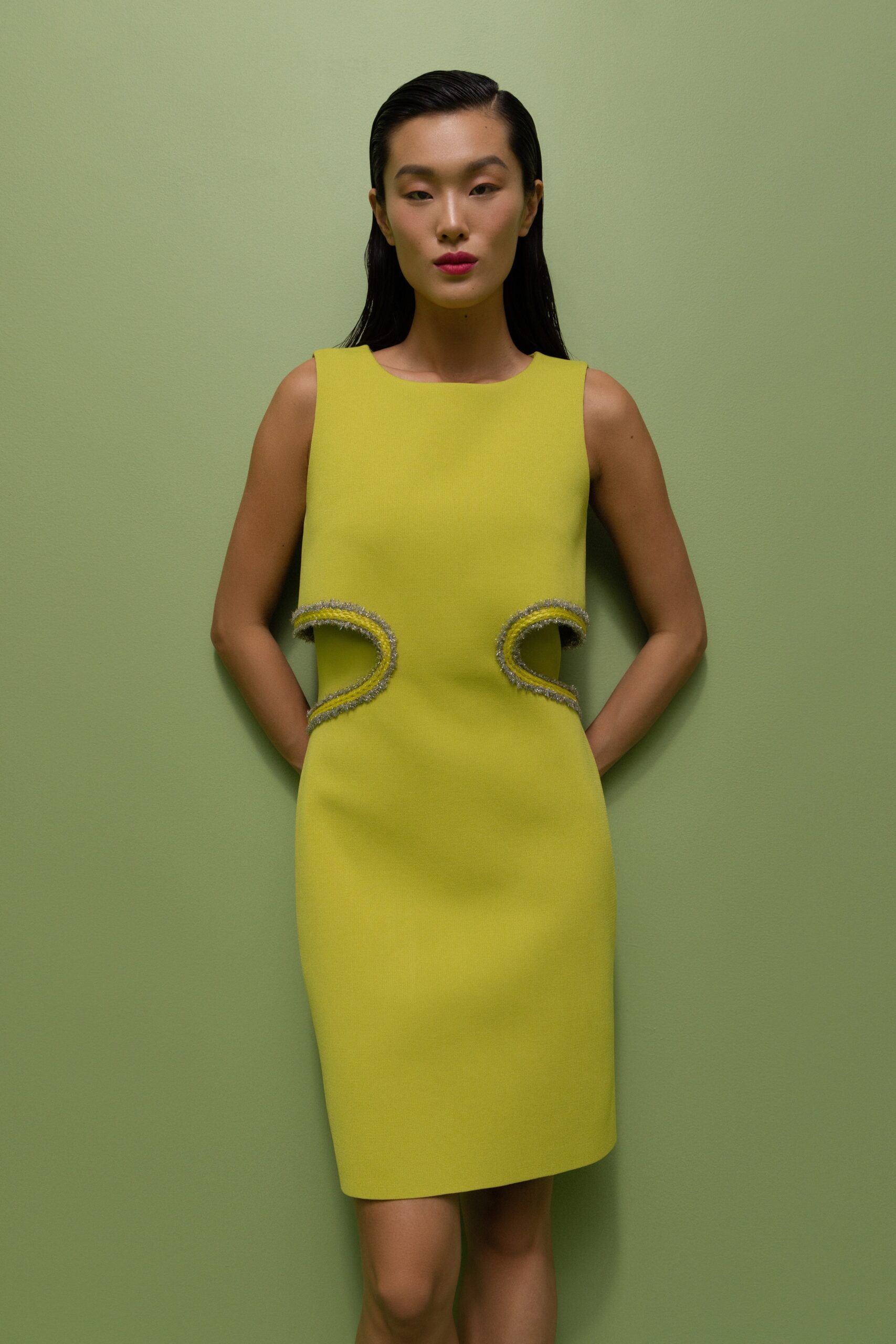 A fitted green sleeveless dress with a high neckline and asymmetric design details.