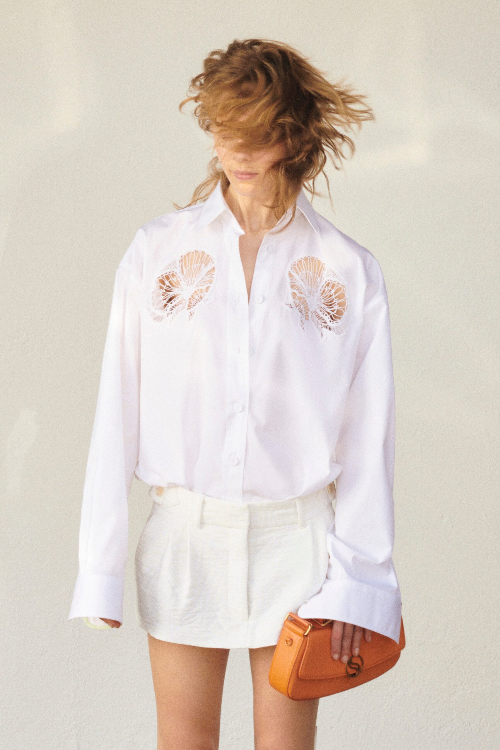 A relaxed white cotton shirt with long sleeves and embroidered details, paired with shorts.