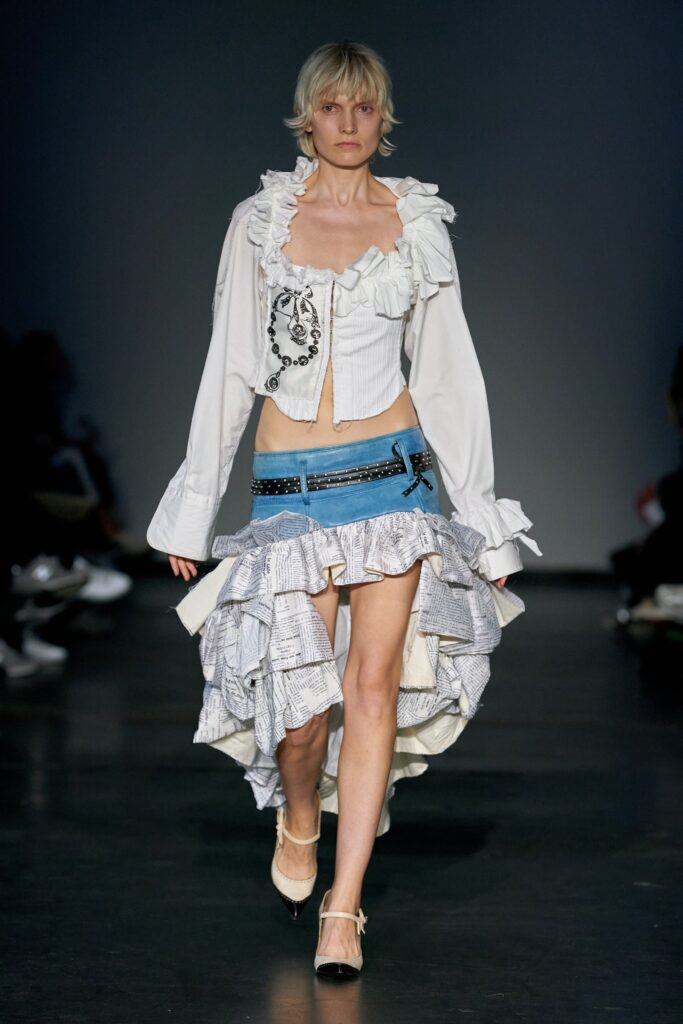 A fitted white long-sleeve ruffled top paired with an asymmetric blue denim skirt.