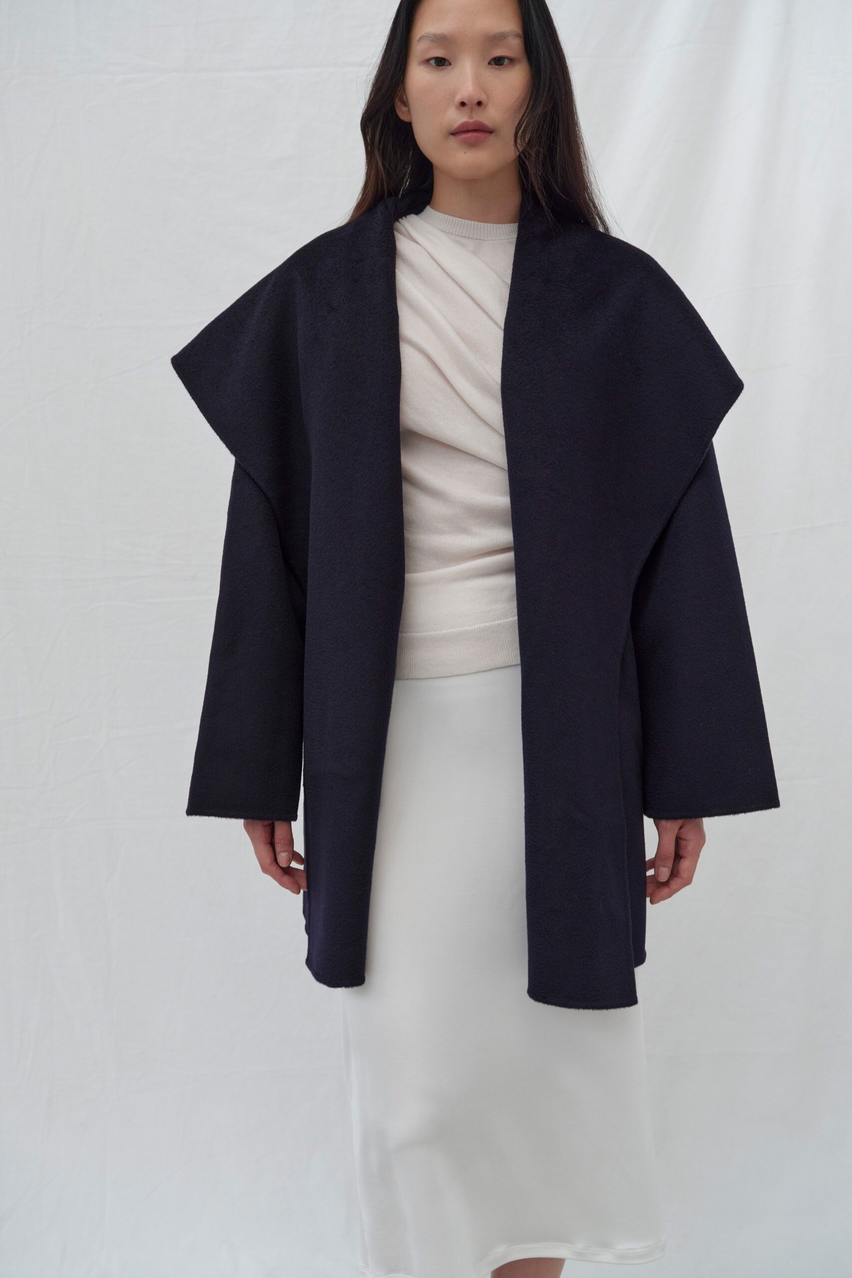 A fitted navy coat layered over a white dress with a high-neck and asymmetric design.