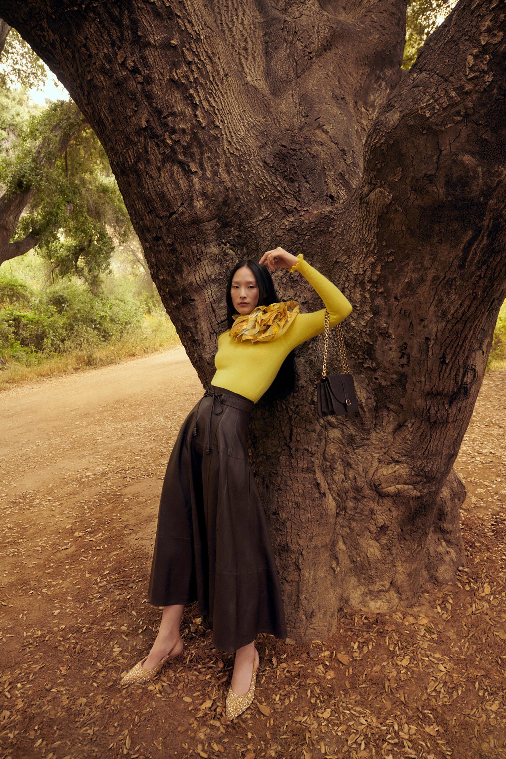 A fitted yellow long-sleeve top with a high neckline paired with a pleated black skirt.