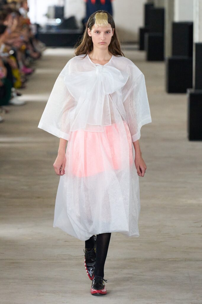 A relaxed white sheer dress with a high neckline and layered design featuring a pink underlayer.