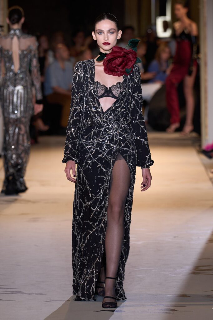 A fitted black silk dress with a V-neckline, long sleeves, and a dramatic slit.