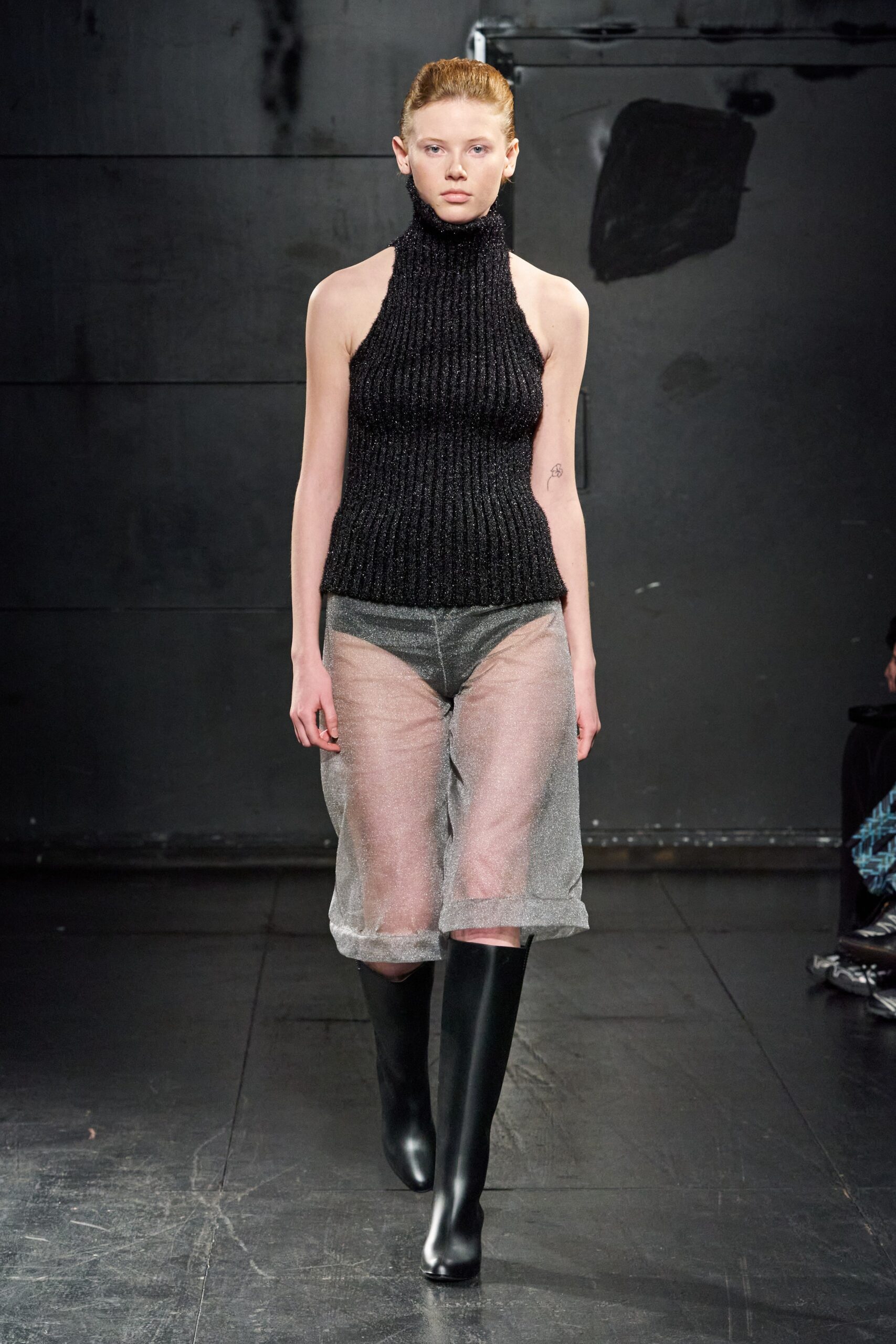 A fitted black sleeveless knit top with a high-neck paired with sheer gray pants.