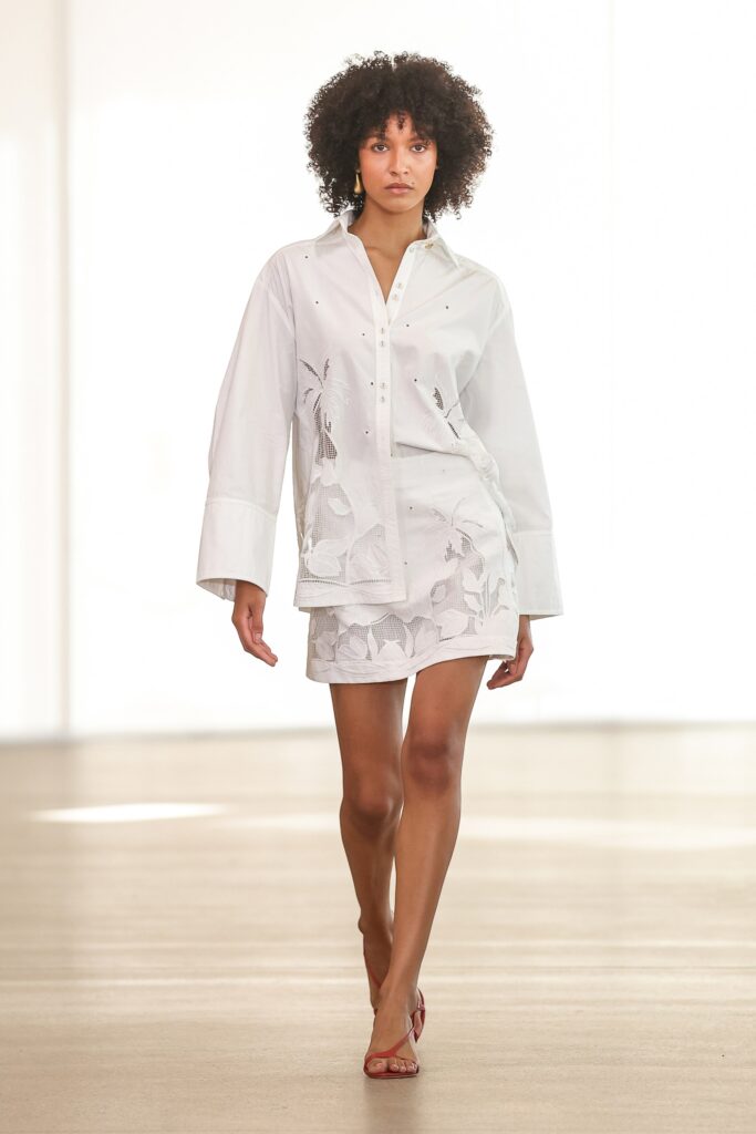 A fitted white cotton shirt with long sleeves and a collared neckline, paired with an embroidered mini skirt.