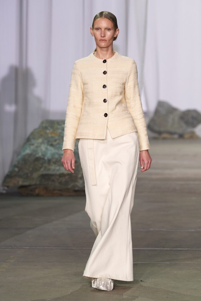 A fitted beige cotton jacket with long sleeves and collared design paired with straight-leg white pants.