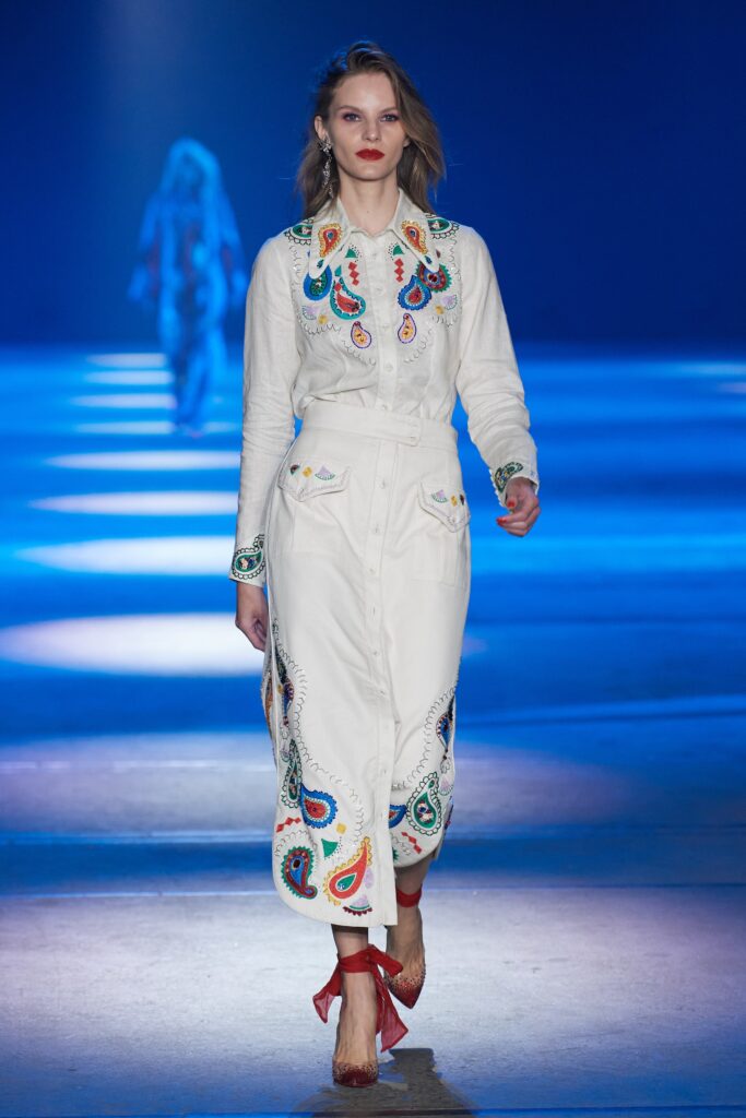 A fitted white cotton dress with long sleeves, a collared neckline, and embroidered details.