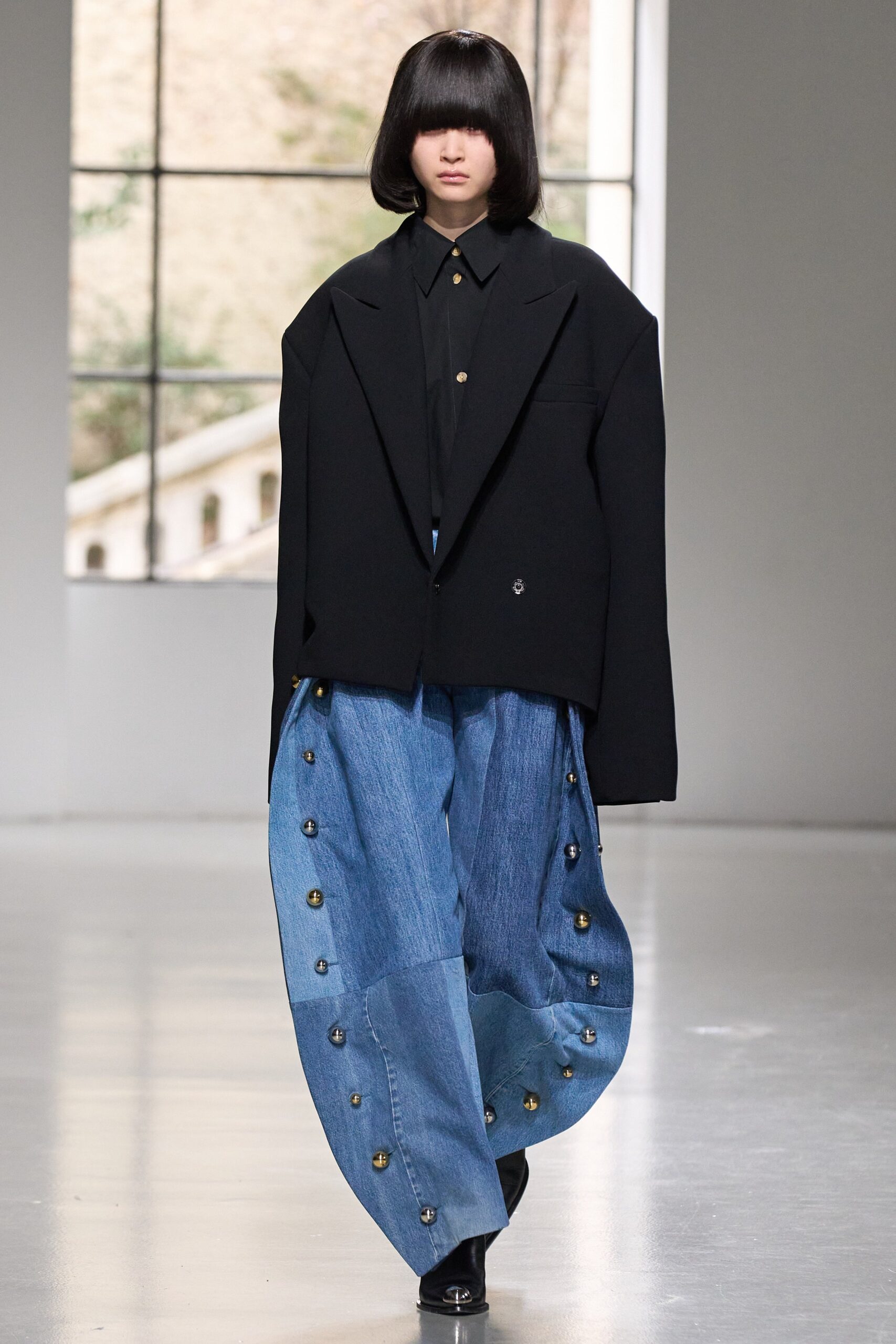 An oversized black jacket paired with wide-leg blue denim pants featuring button details.