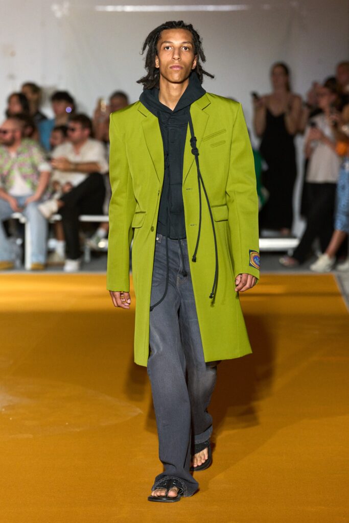 A relaxed fit green coat paired with gray pants, featuring a hood and button details.