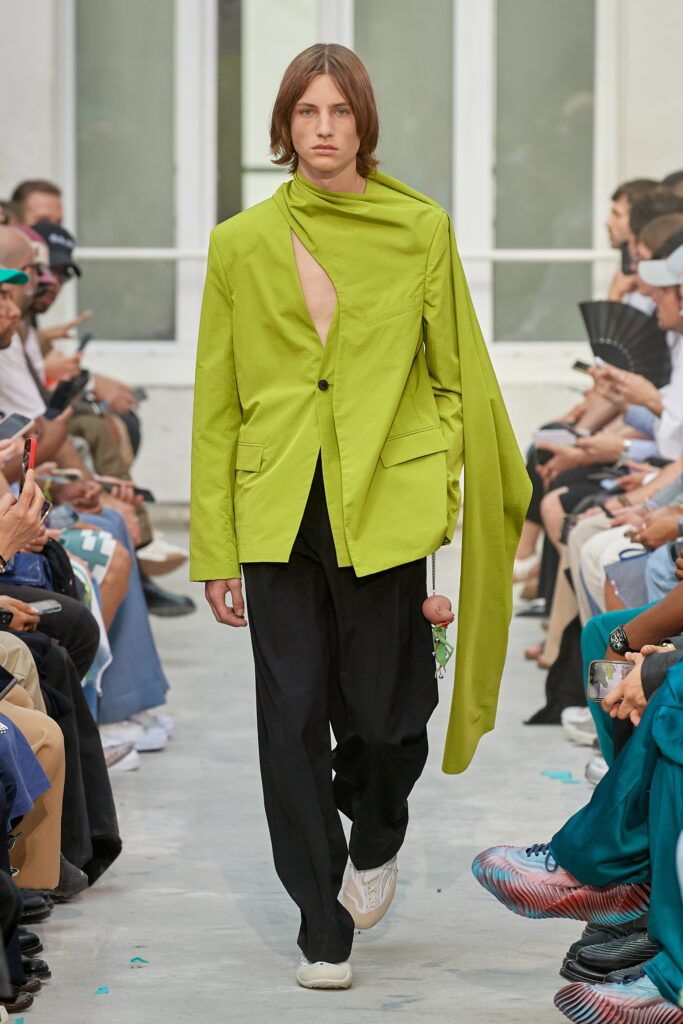 A relaxed green jacket with an asymmetric design paired with black pants.