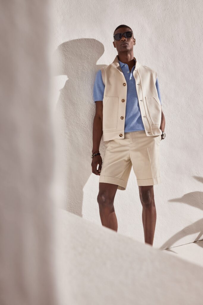 A relaxed beige cotton vest paired with a blue collared short-sleeve shirt and beige shorts.