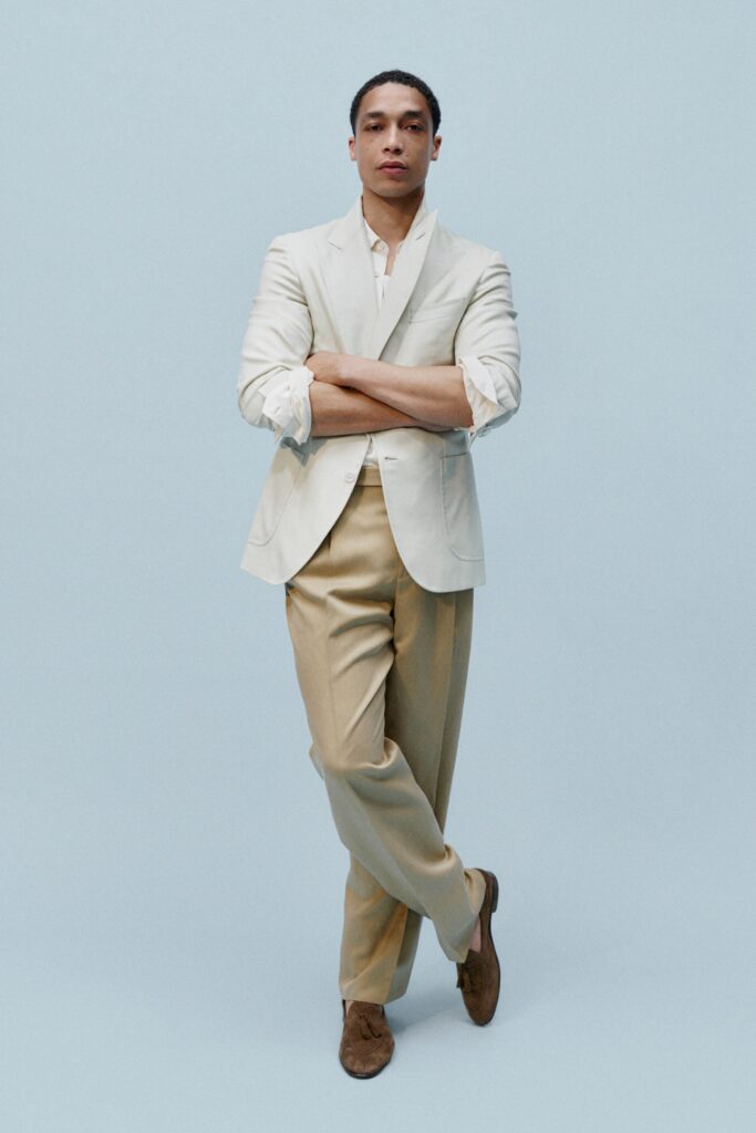 A tailored beige cotton blazer with long sleeves and buttoned details, paired with cream trousers.
