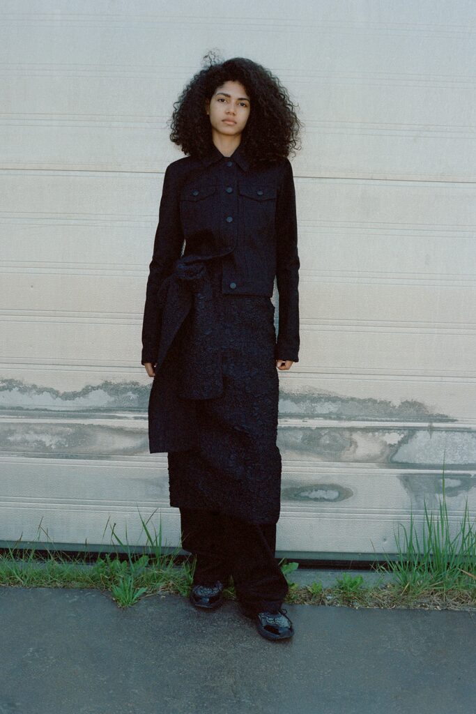 A fitted black jacket with long sleeves and a collared design paired with an asymmetric layered skirt.