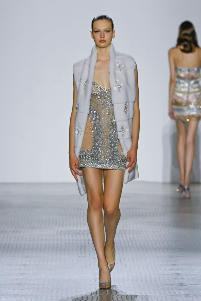 A fitted silver sequined mini dress layered with a sleeveless white fur coat.