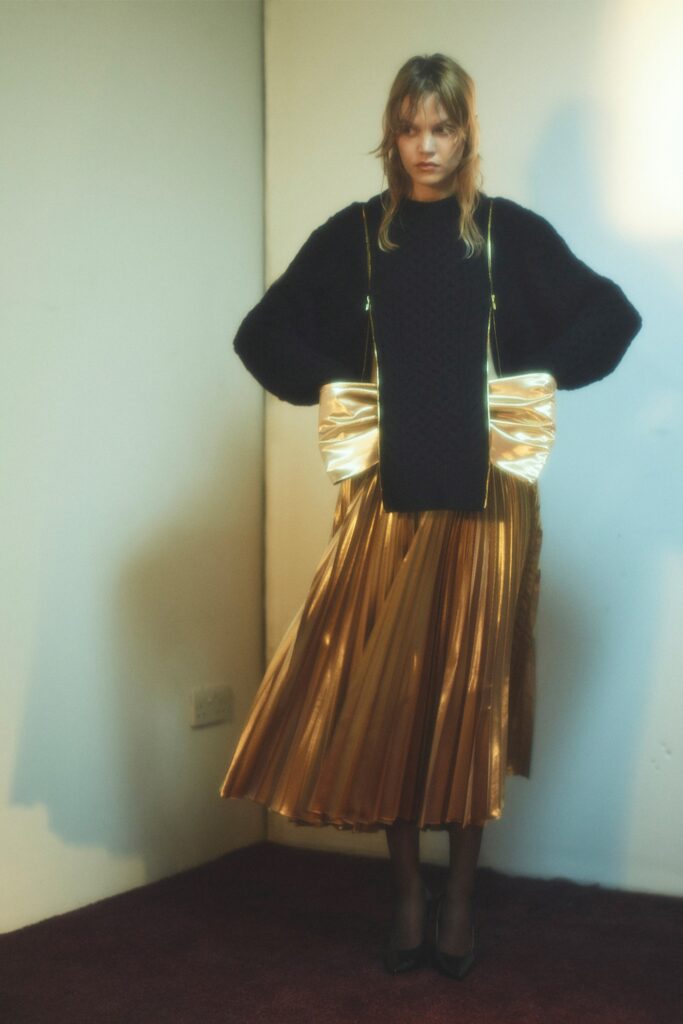 A relaxed black top with long sleeves paired with a pleated gold skirt.