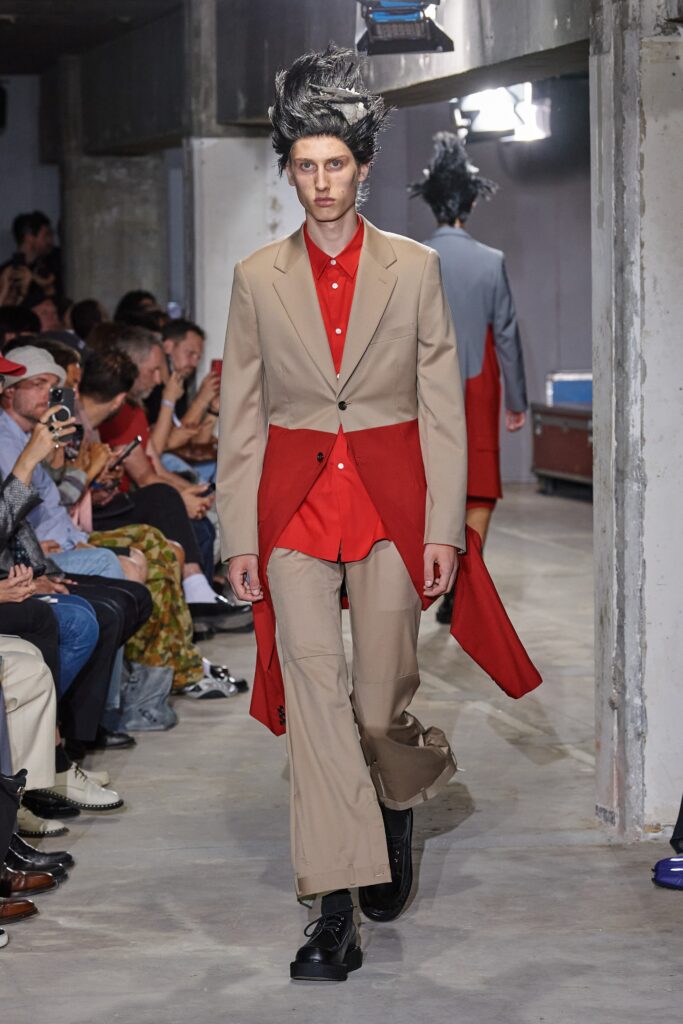 A tailored beige suit featuring a long-sleeve collared red shirt with an asymmetric design.