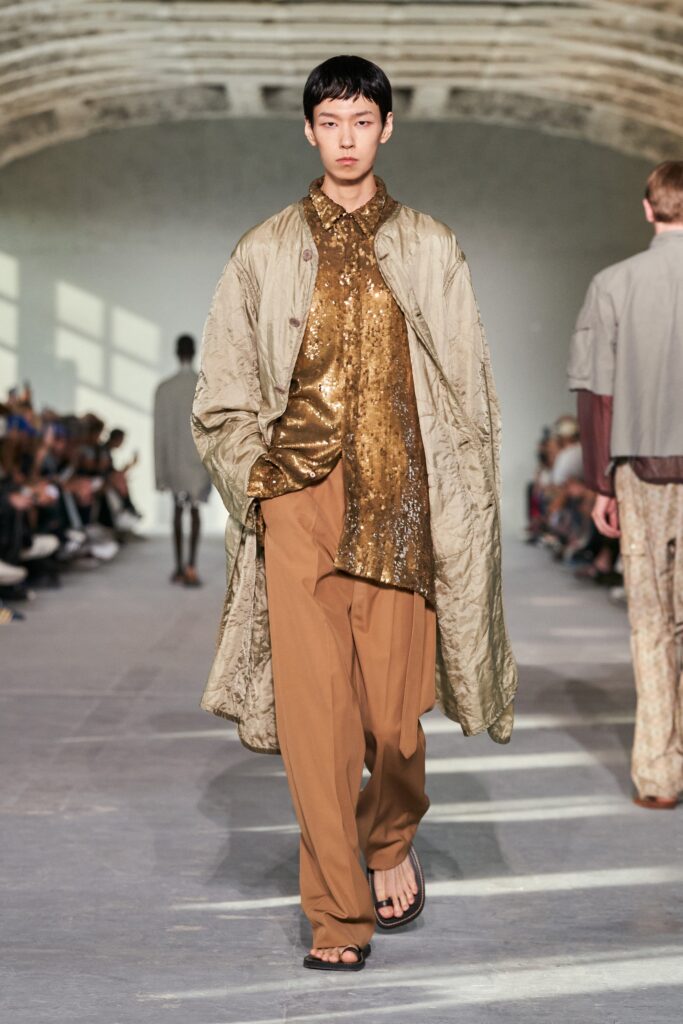 A relaxed beige coat layered over a gold sequined collared shirt.