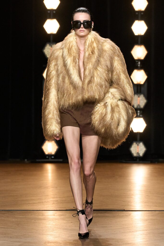 A fitted brown fur coat worn over shorts, showcasing a sleeveless design.