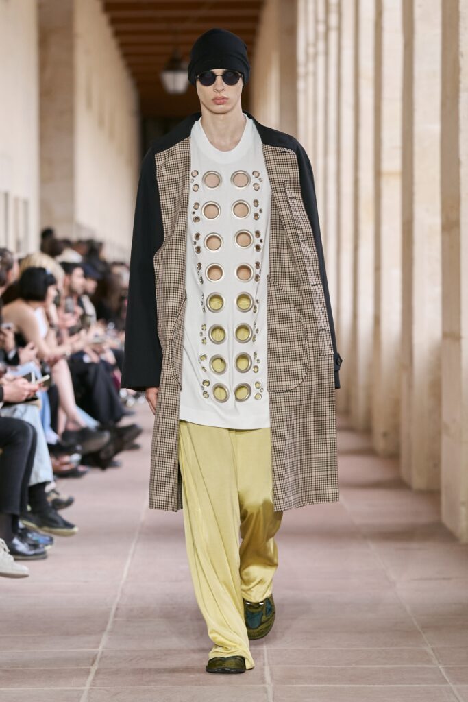 A relaxed black coat layered over a printed top with yellow pants.