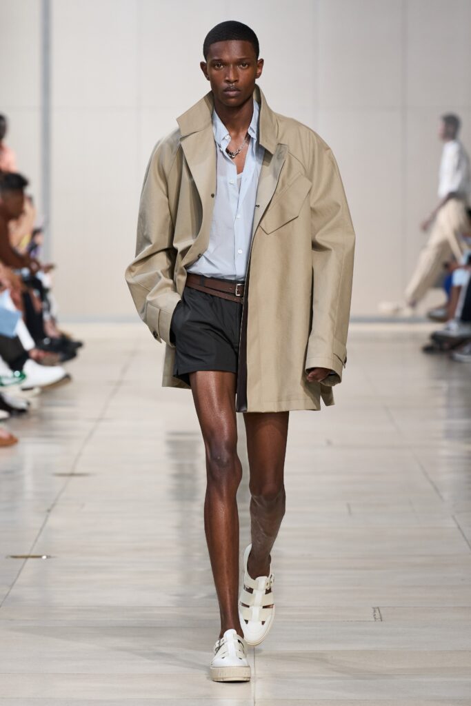 An oversized beige jacket with a collared neckline paired with black shorts.
