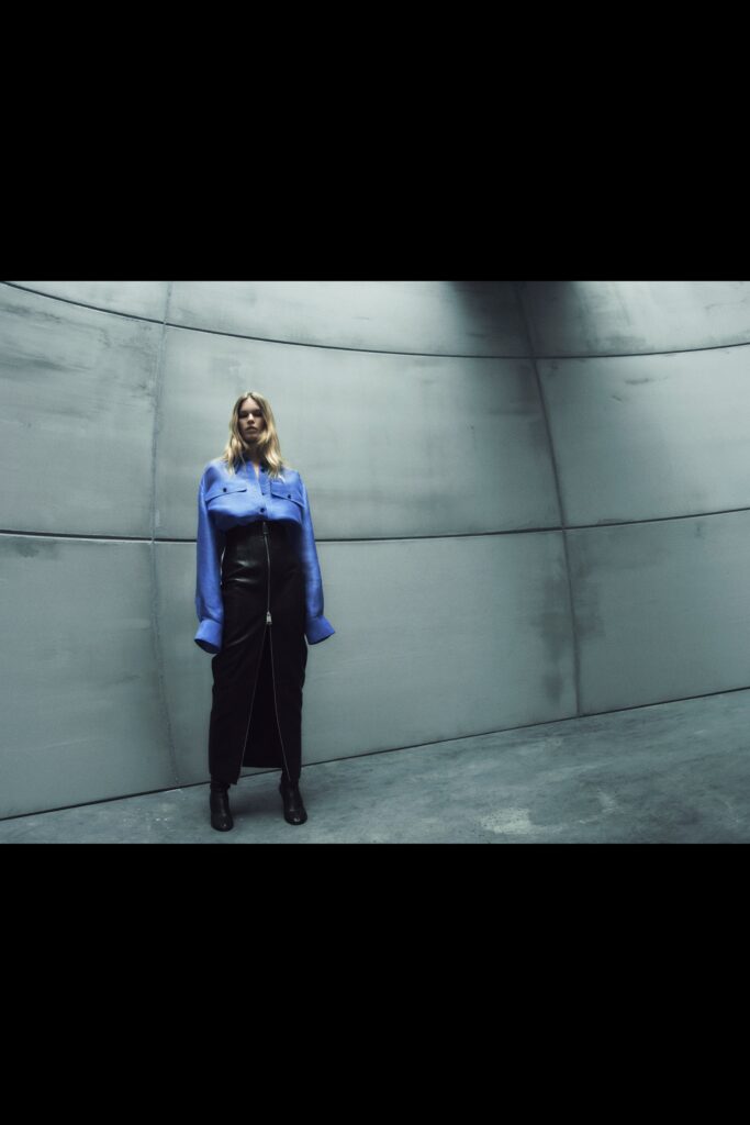 A fitted blue long-sleeve shirt with a collared neckline paired with a fitted black zippered skirt.