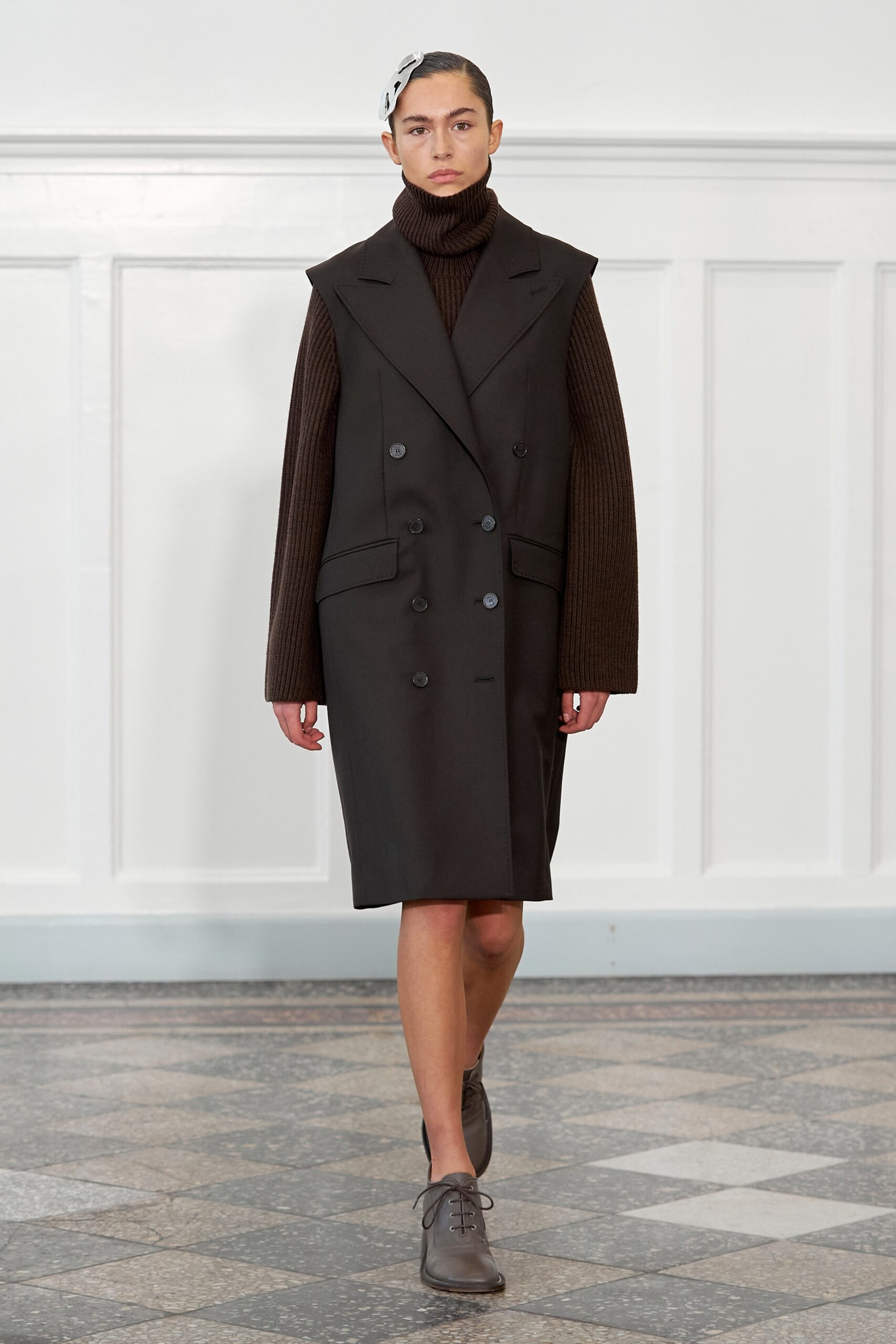 A fitted black wool coat dress with long sleeves and an asymmetric buttoned design.