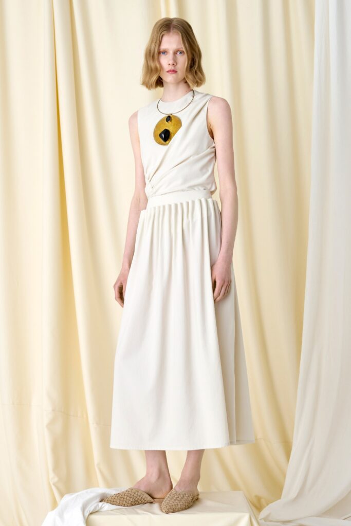 A relaxed white sleeveless dress with a high neckline and tiered design.