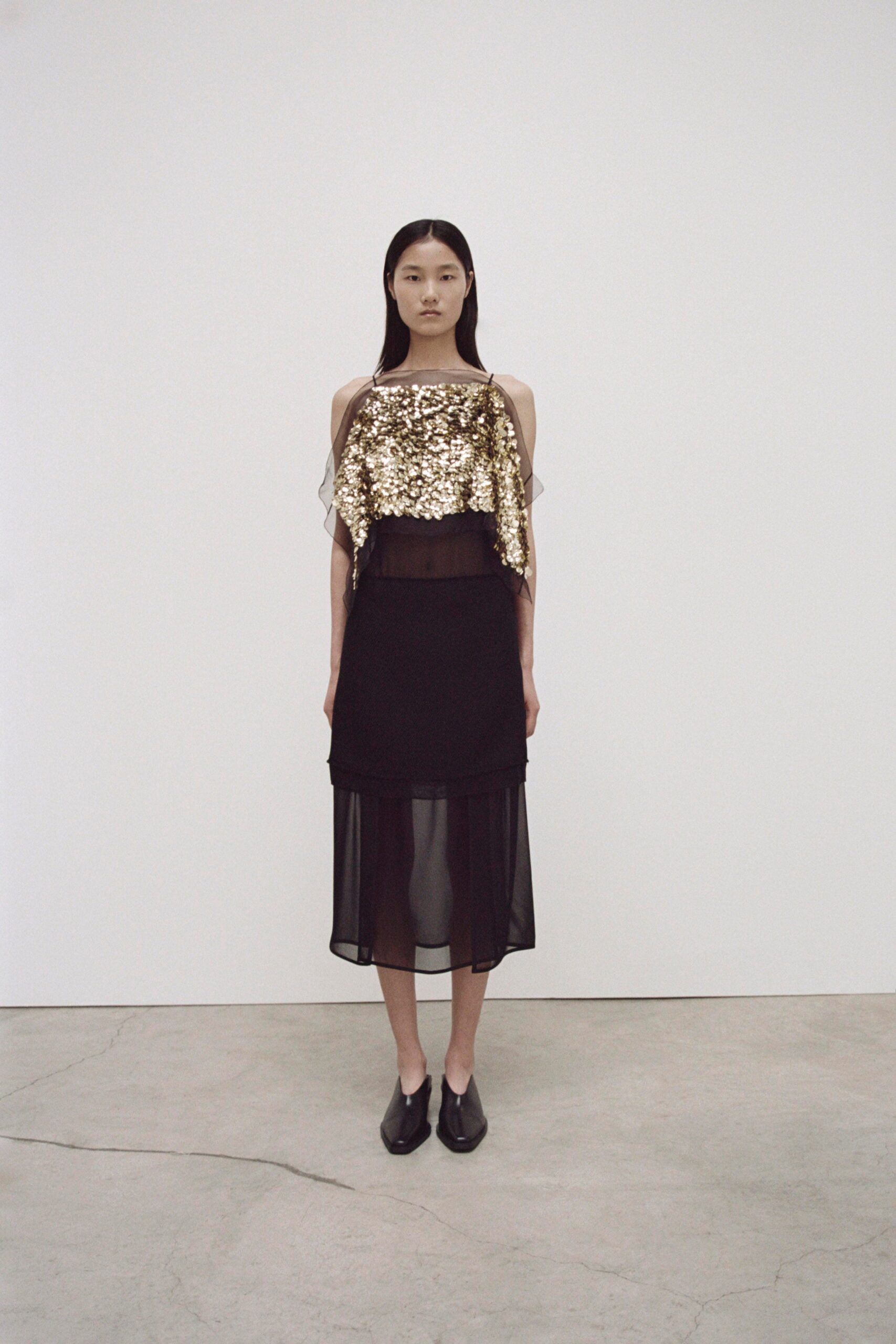 A fitted black sheer top with sequined details and a layered black skirt.