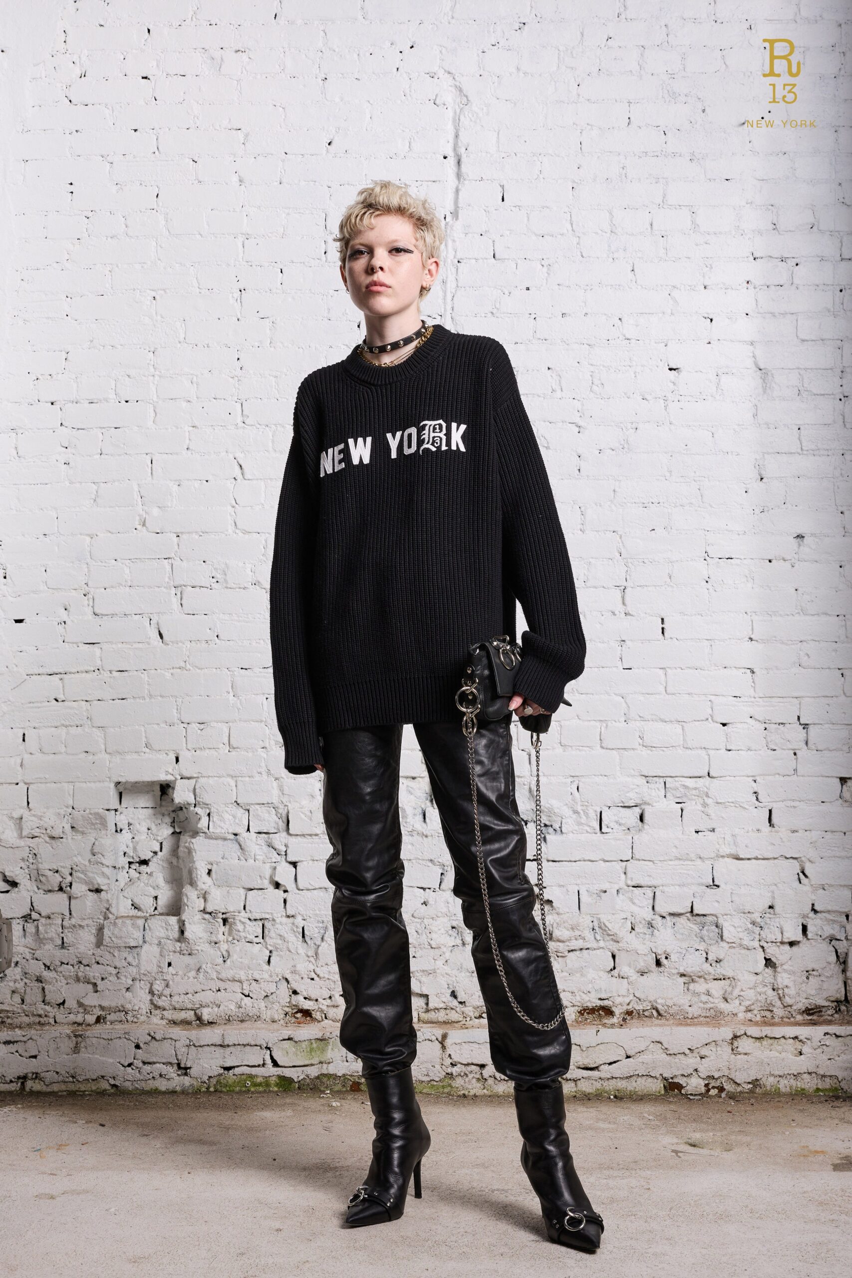 An oversized black sweater with a printed design paired with fitted black leather pants.