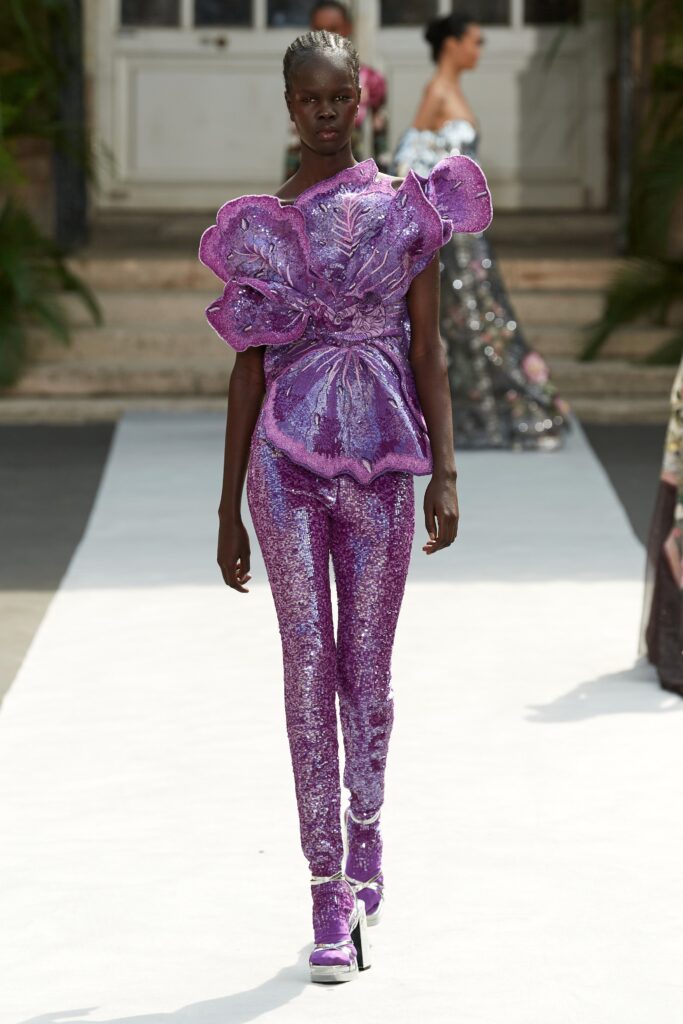 A fitted purple sequin top with long sleeves and high-neck paired with flared pants.